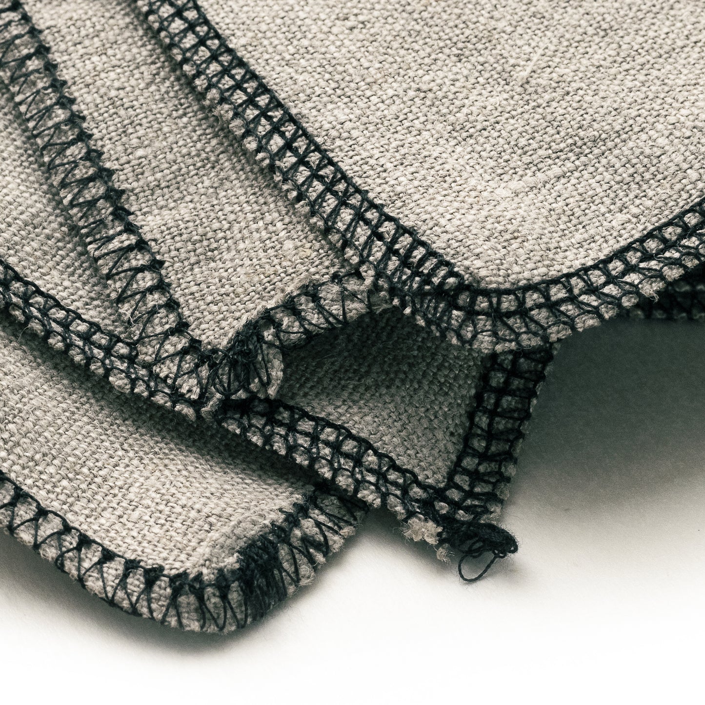 Close-up of a folded No.9 linen applicator cloth with black sewn edges on a white background.