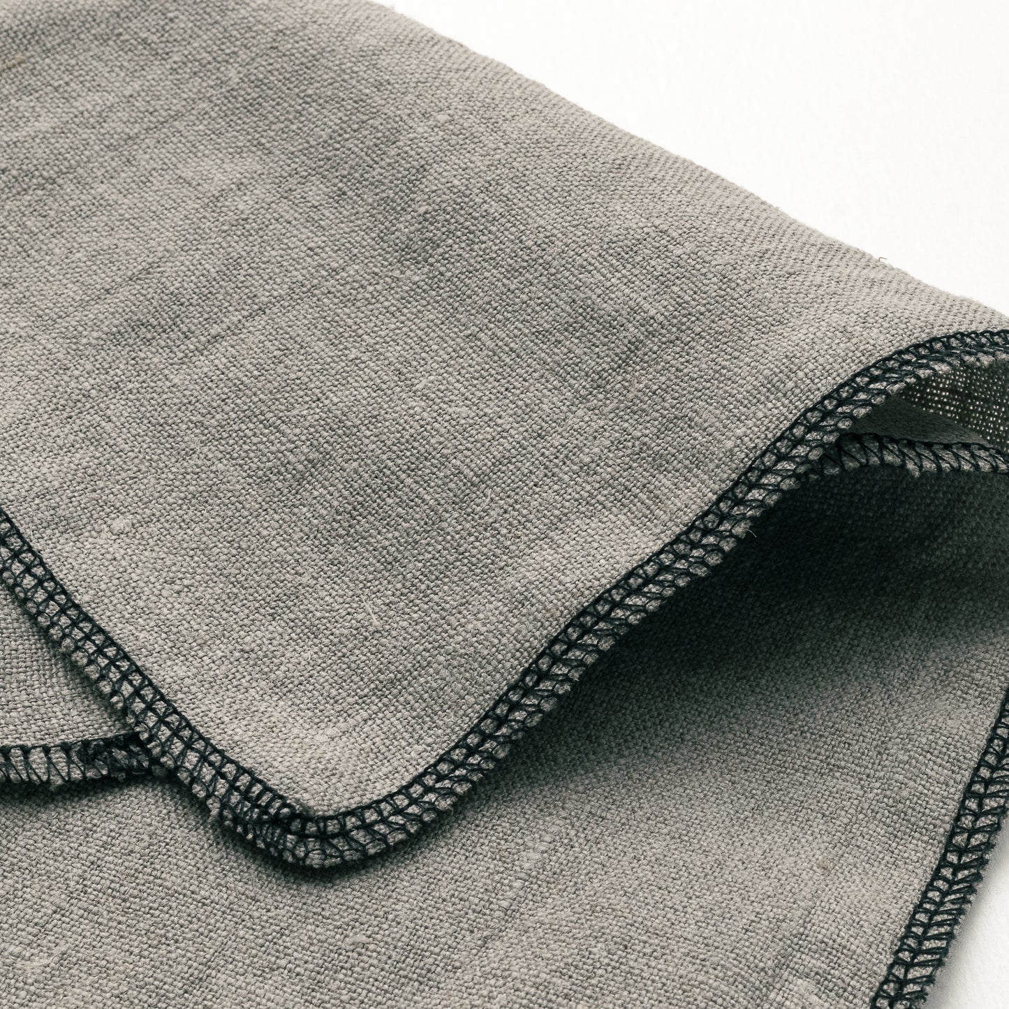 Close-up of a folded No.9 linen applicator cloth with black sewn edges on a white background.