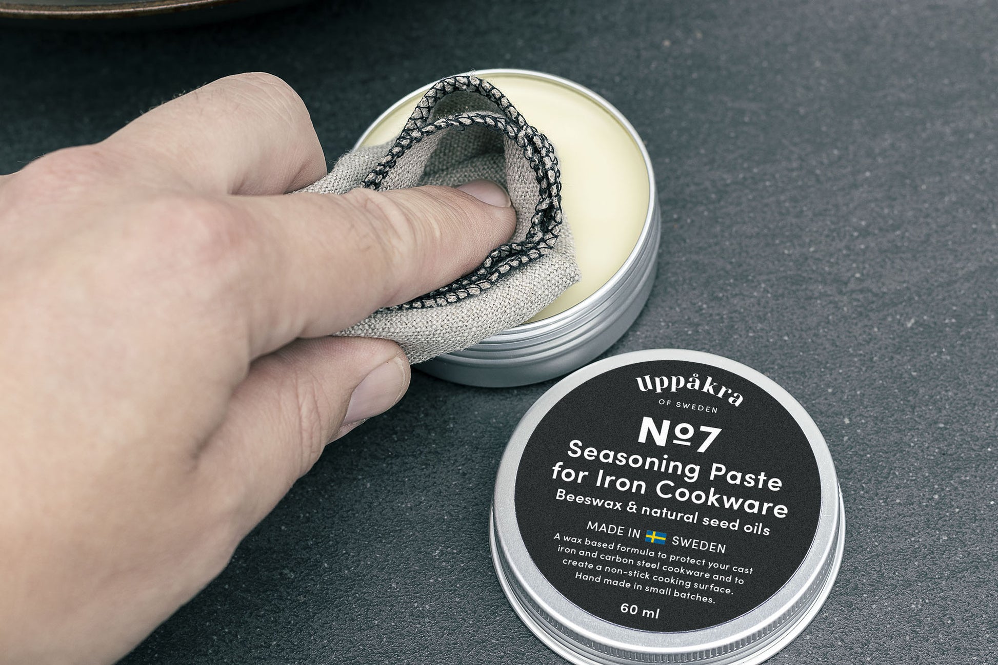 A hand using the No.9 Applicator cloth to apply wax from an open jar of Seasoning Paste.