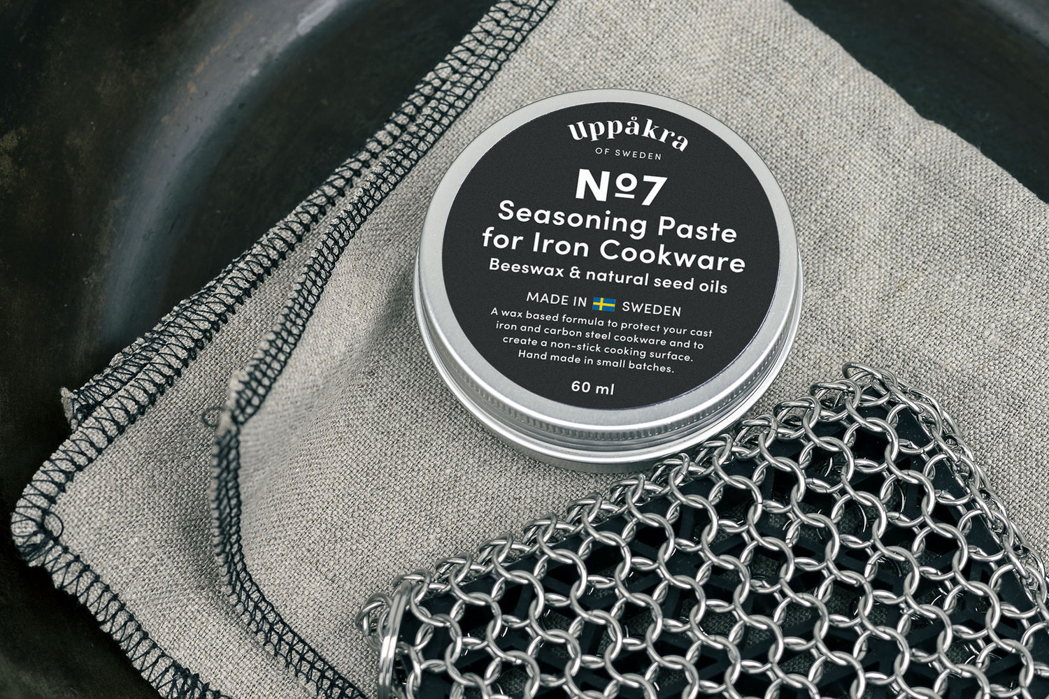 A jar of No.7 Seasoning Paste on a linnen cloth next to a chainmail scouring pad in a frying pan.